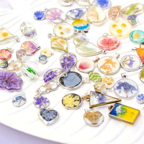 A collection of handmade epoxy jewelry pendants with real flowers and plants inside and resting on white stand