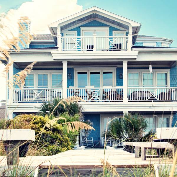 The exterior of a vacation rental house on a beach. The house is blue and white with different patio spaces.